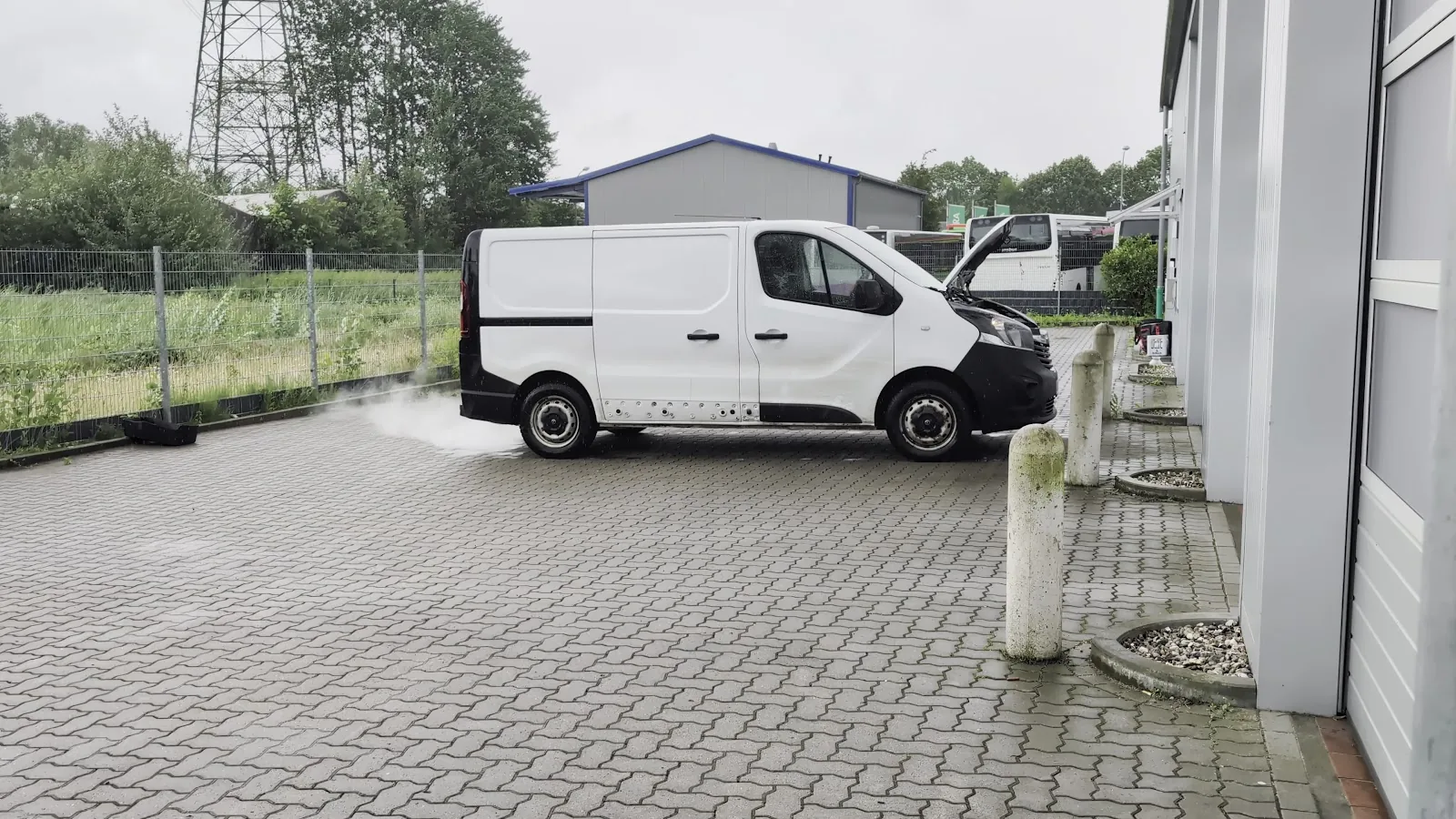 Weißer Transporter auf dem Hof der AZB Werkstatt, aus dem Auspuff tritt Reinigungsnebel in eine Auffangwanne am Boden