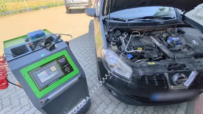 Schwarzer Nissan mit geöffneter Motorhaube, angeschlossen an das grüne mobile Reinigungsgerät auf dem Hof