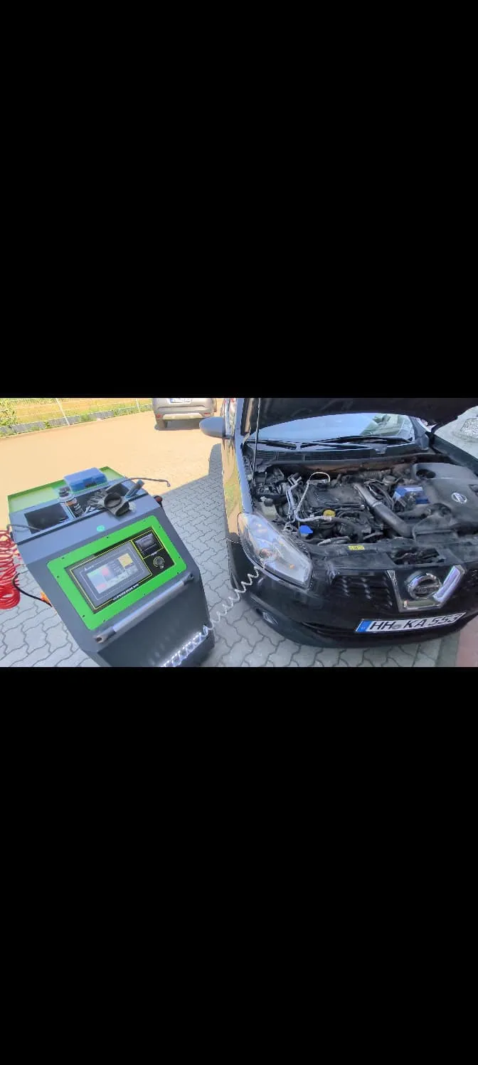 Schwarzer Nissan mit geöffneter Motorhaube, angeschlossen an das grüne mobile Reinigungsgerät auf dem Hof