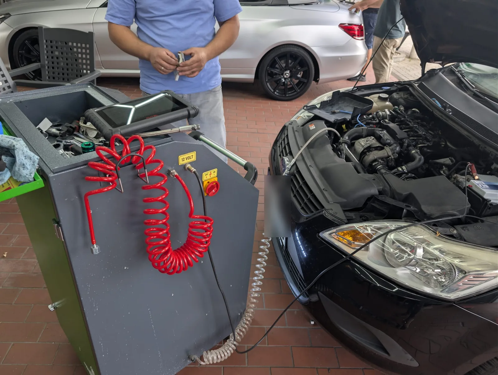 Reinigungsgerät und Diagnosetablet neben einem schwarzen Mercedes mit geöffneter Motorhaube
