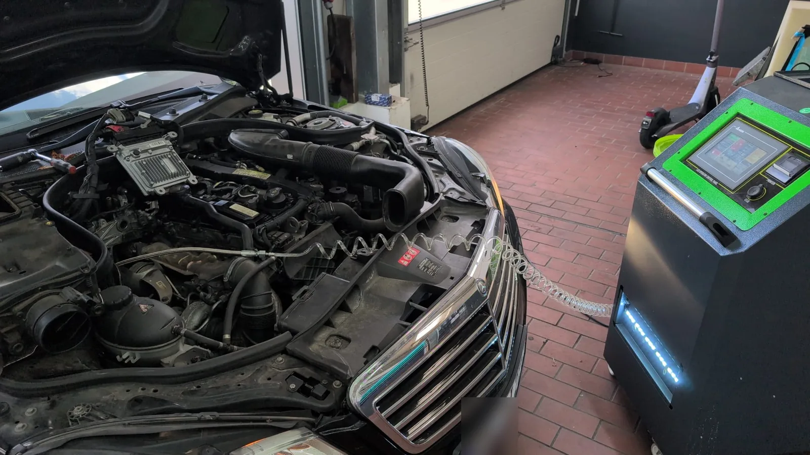 Mercedes in der Werkstatthalle, Motorraum offen und über einen Schlauch mit dem Reinigungsgerät verbunden