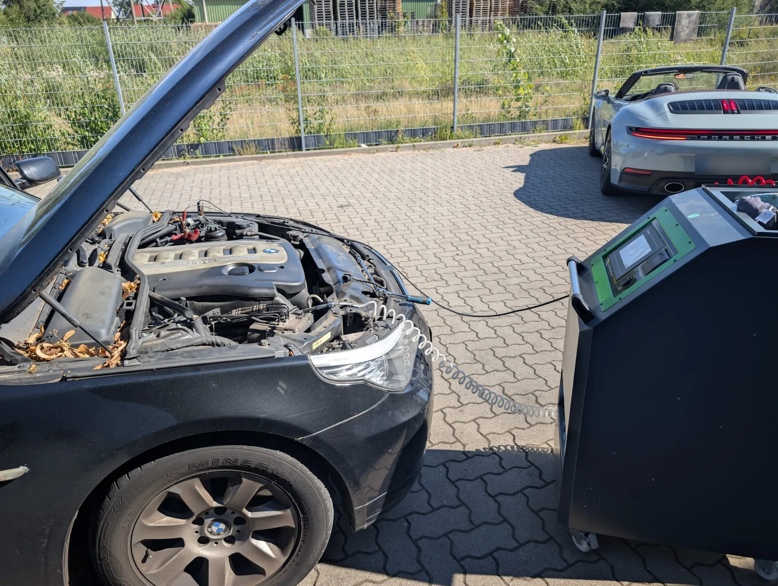 Dunkler BMW mit geöffneter Motorhaube am Reinigungsgerät auf dem Hof der AZB Werkstatt